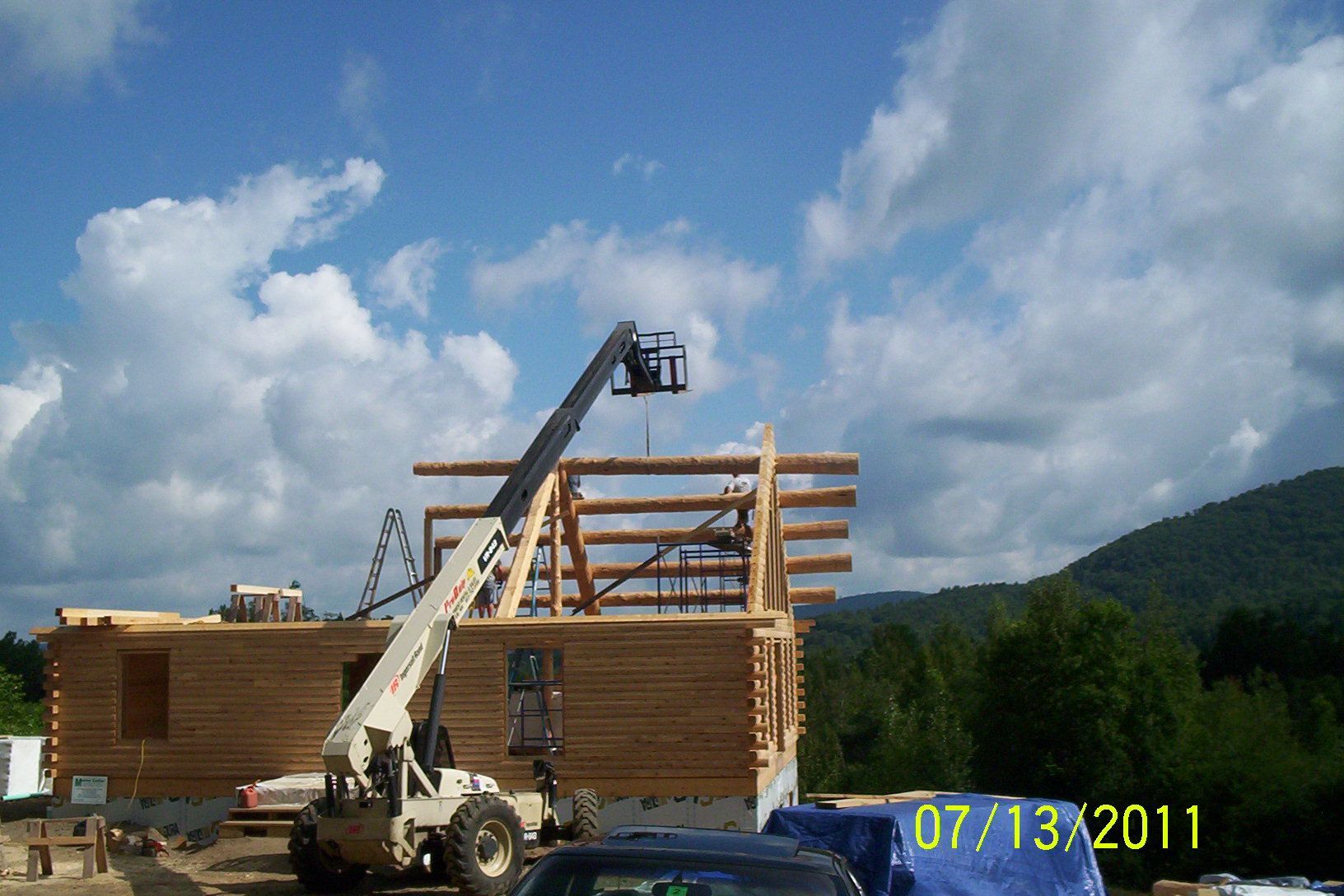 Construction site with a crane lifting lumber beams beside a partially built wooden structure under a cloudy sky