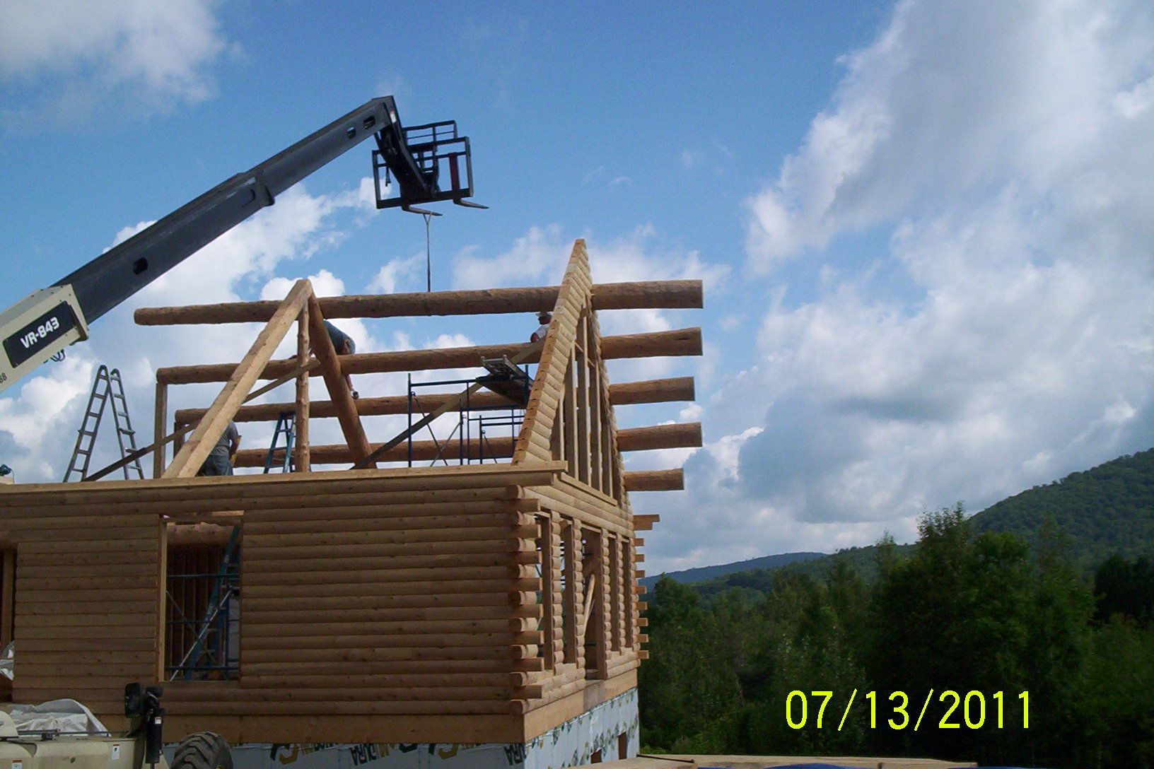 Wooden house frame under construction with a crane lifting beams, dated 07/13/2011