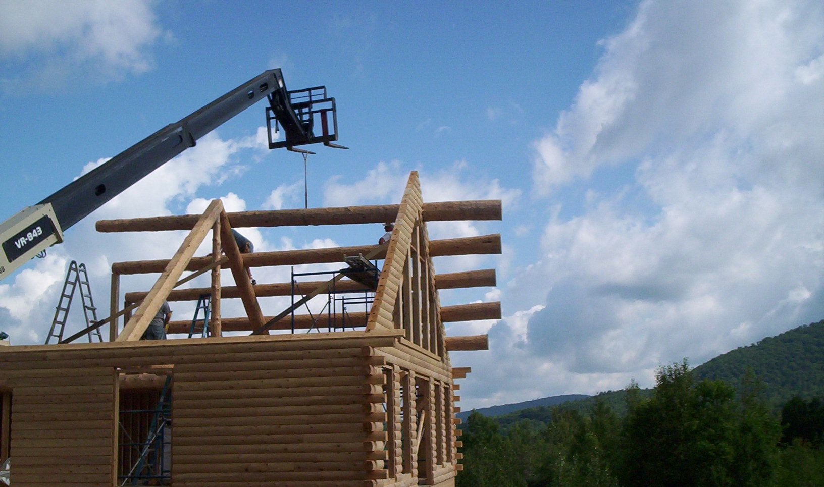 Crane lifting a wooden log cabin frame under construction against a blue sky