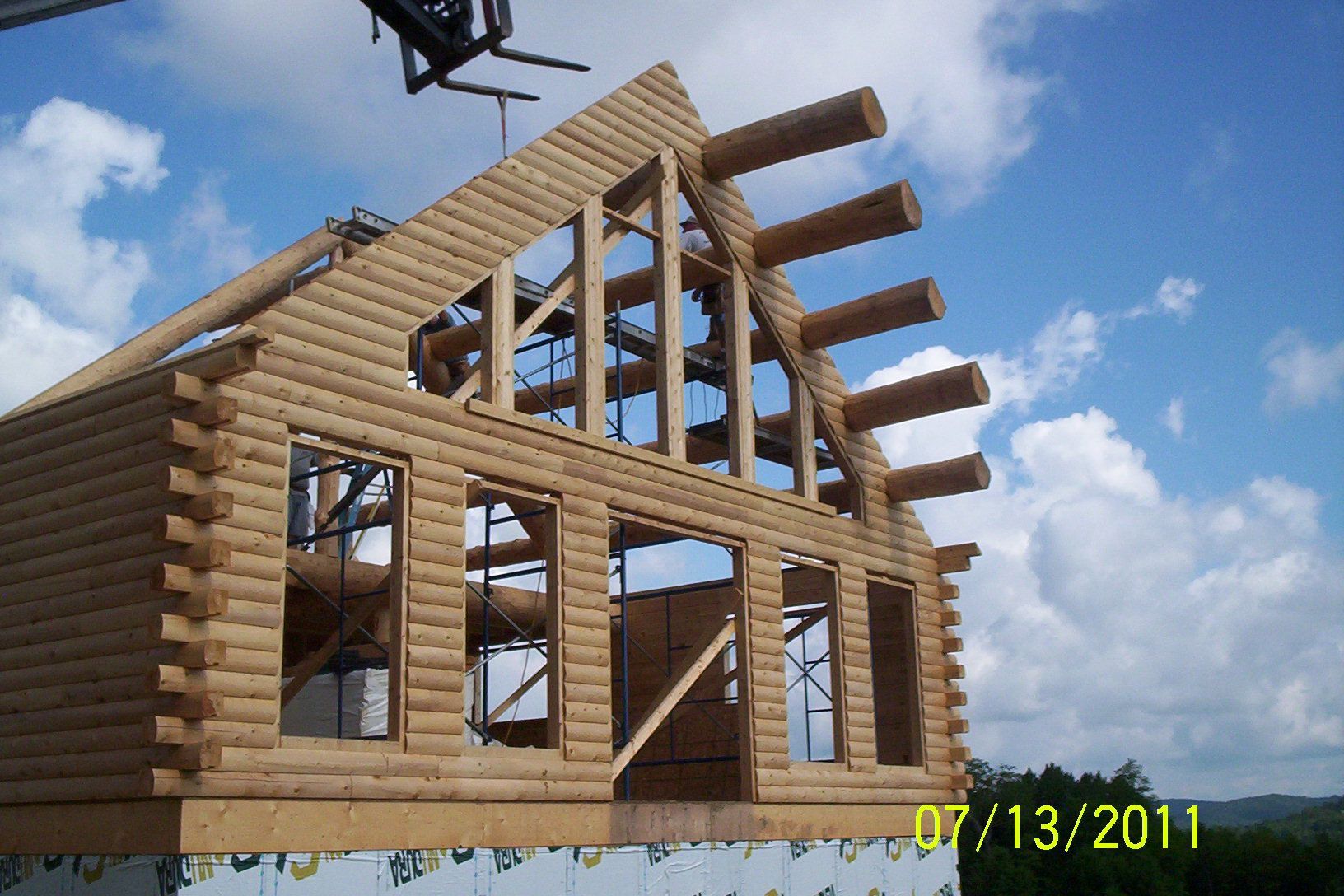 Partially built log cabin frame under a blue sky with clouds