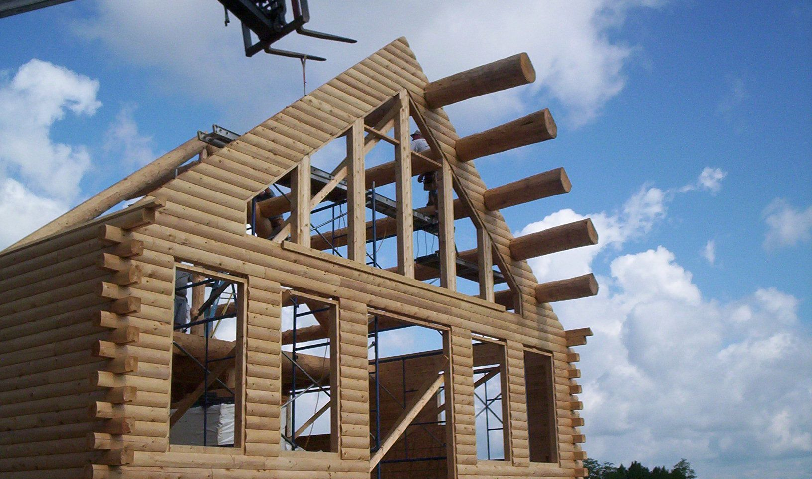 Partially built log cabin frame with exposed wooden beams against a blue sky