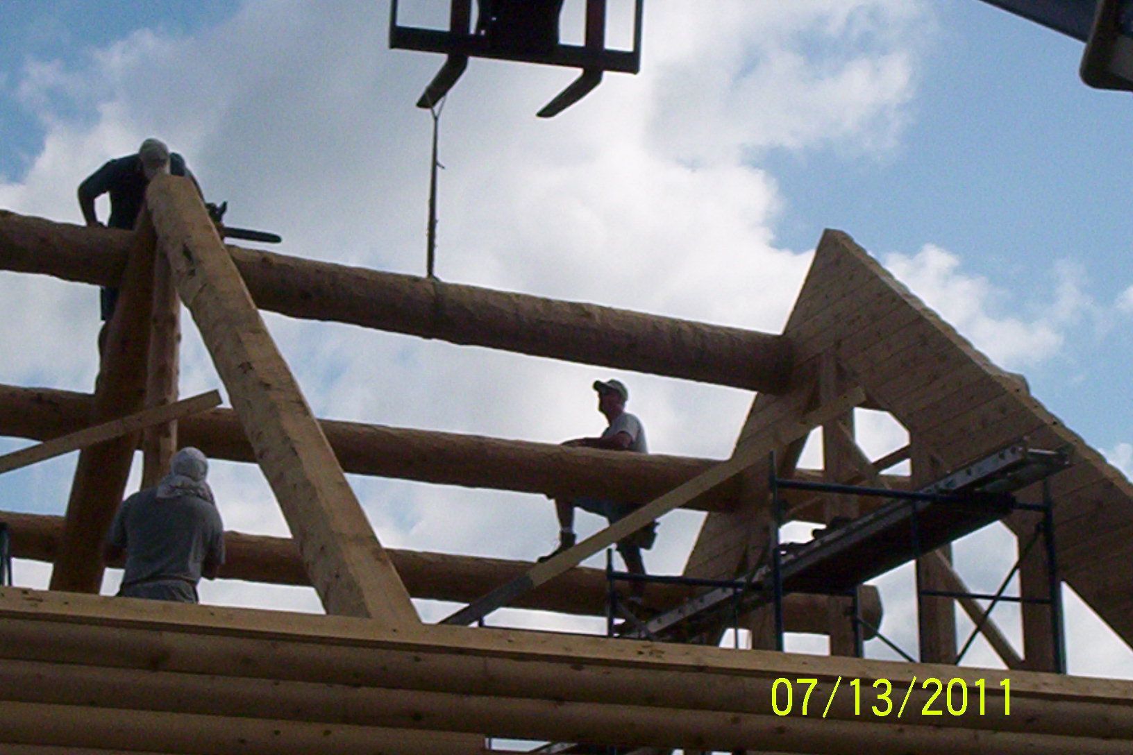 Workers on a wooden roof frame under construction against a cloudy sky.
