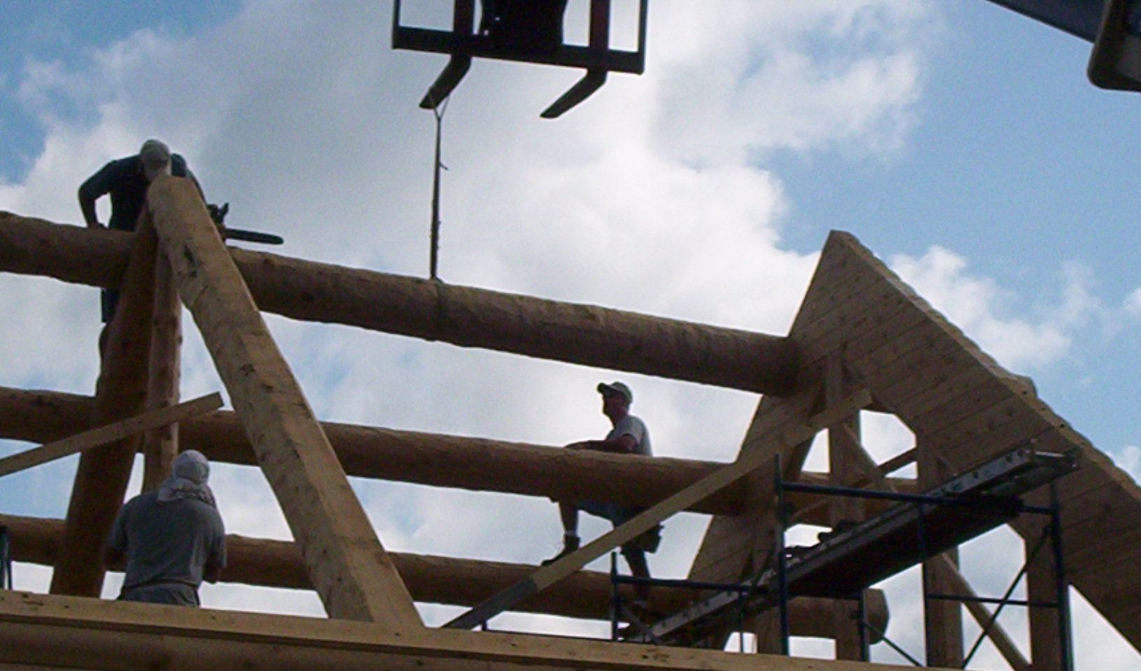 Workers on a wooden construction frame with triangular supports under a partly cloudy sky