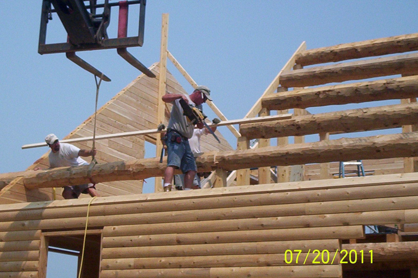 Workers installing wooden roof trusses on a house frame under a clear blue sky