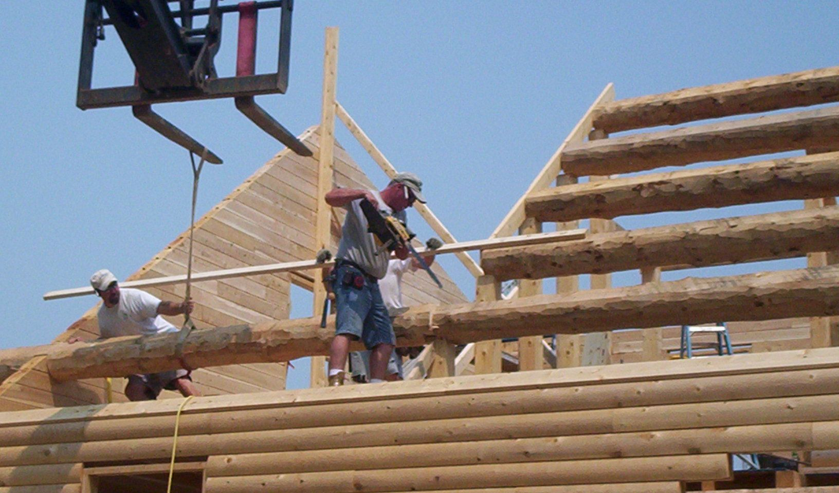 Workers building a wooden roof frame on a construction site under a blue sky