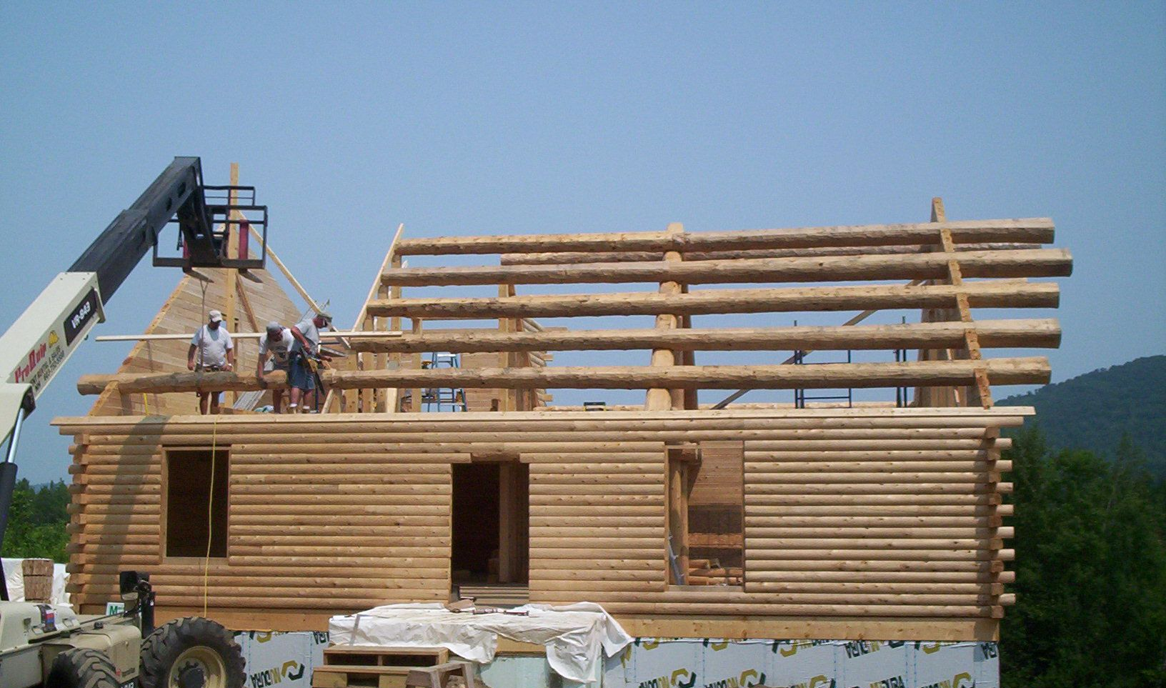 Workers building a wooden house frame with a crane lifting materials on a sunny site