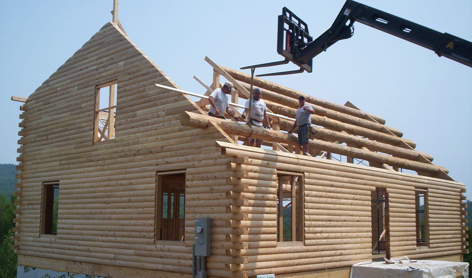 Workers installing logs on a house under construction, with a crane lifting materials.