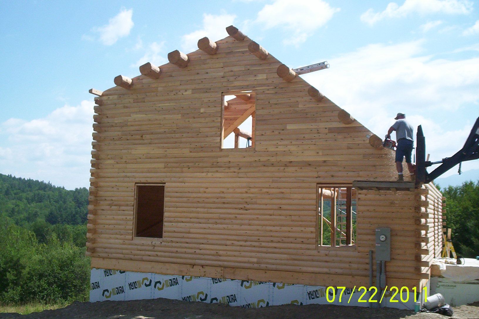 Wooden house under construction with a worker on the roof and blue sky behind it