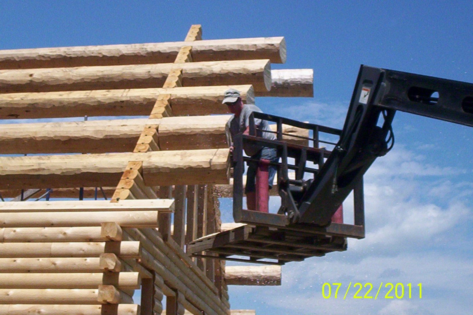 Construction worker in a lift installing logs on a wooden frame under a blue sky