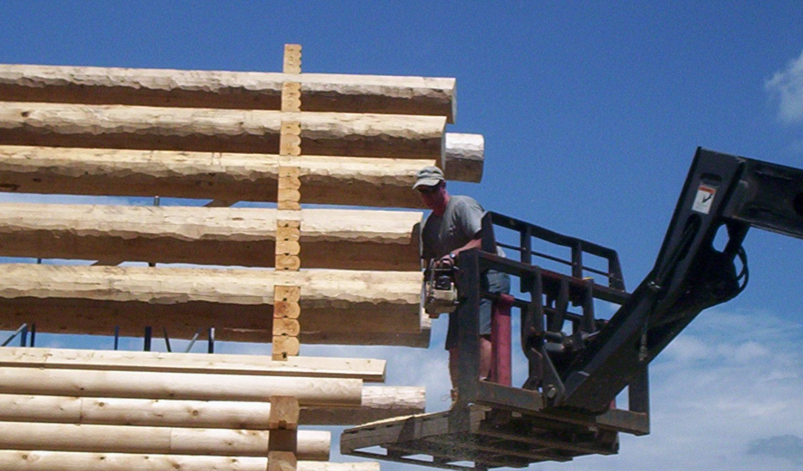Forklift stacking logs outdoors against a blue sky