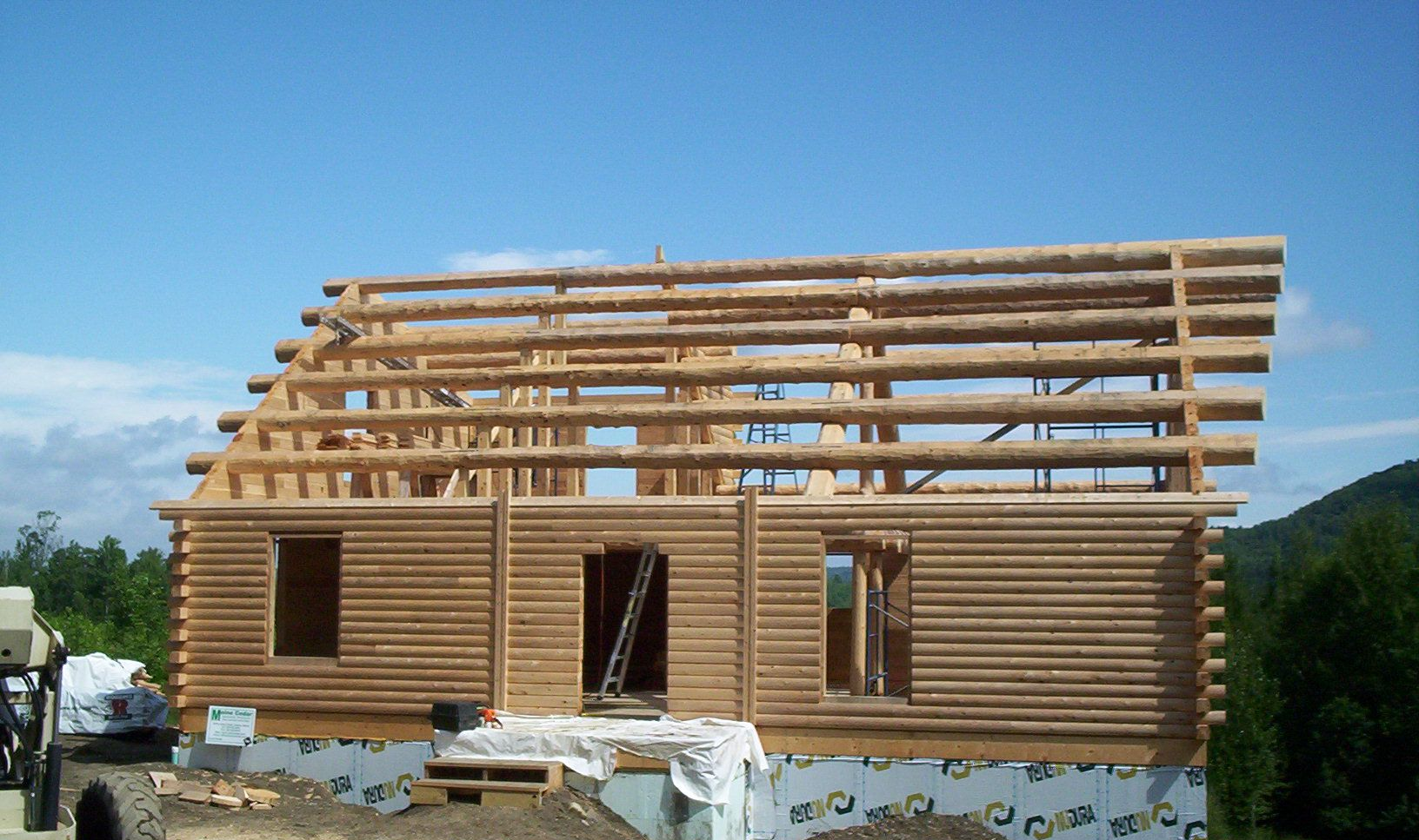 Partially built wooden house frame with roof beams under construction on a sunny site