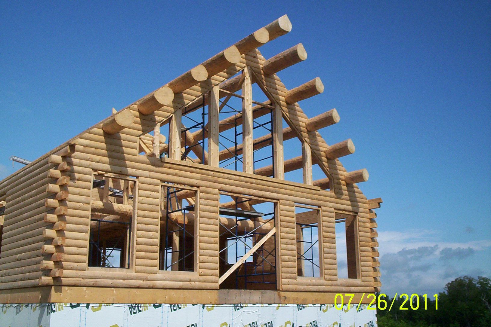 Partially built log cabin with exposed roof framing under a clear blue sky