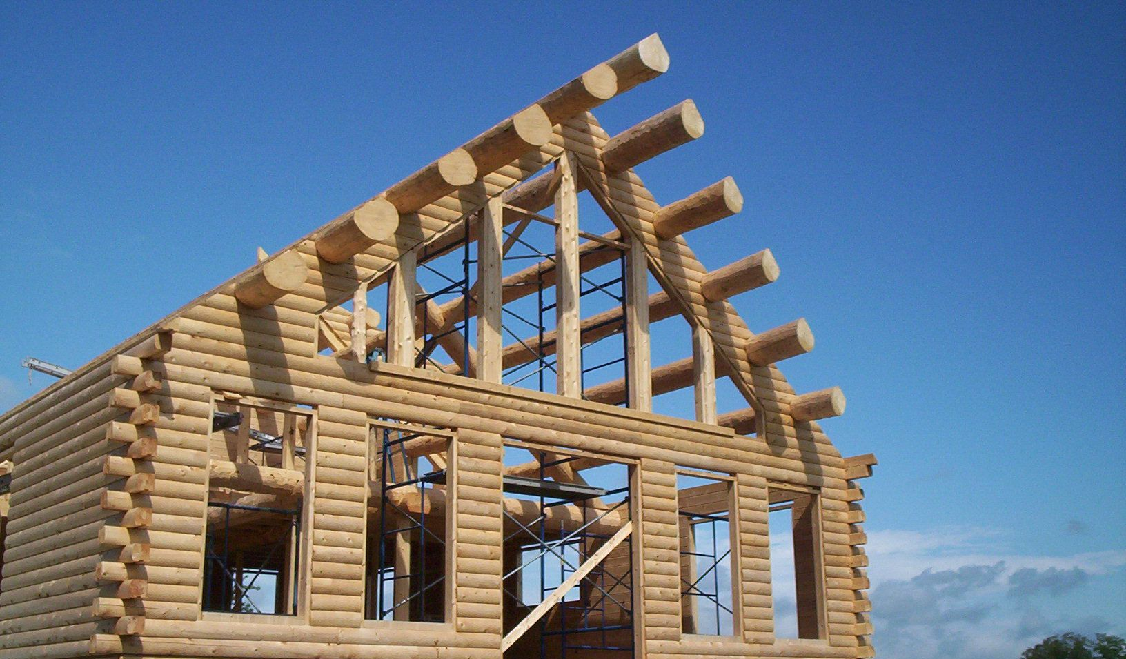 Partially built wooden log cabin frame under a clear blue sky
