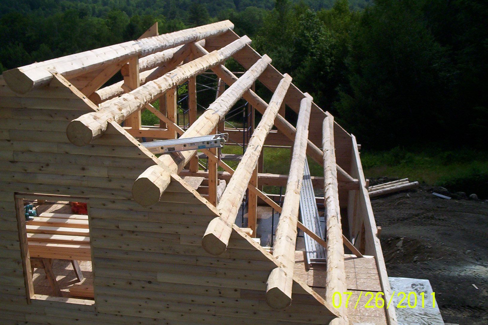 Wooden house frame under construction with exposed roof trusses and boarded walls outdoors.