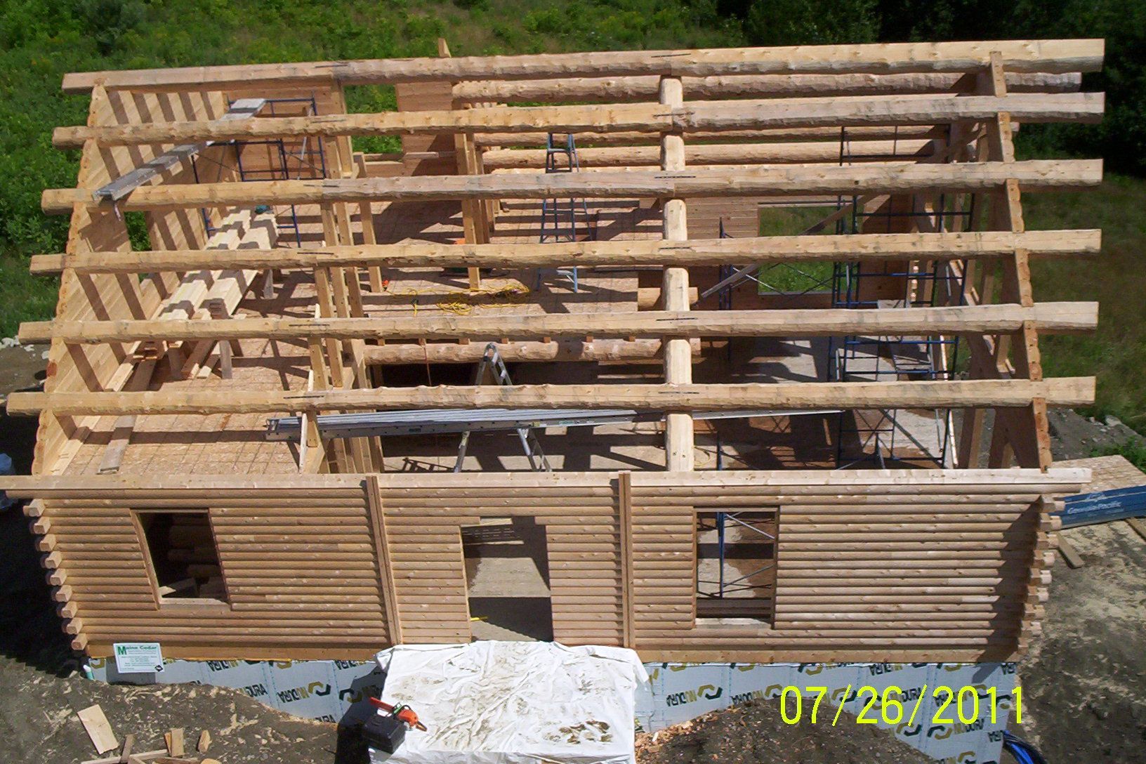 Partially built wooden house frame with roof beams and slatted walls in a construction site