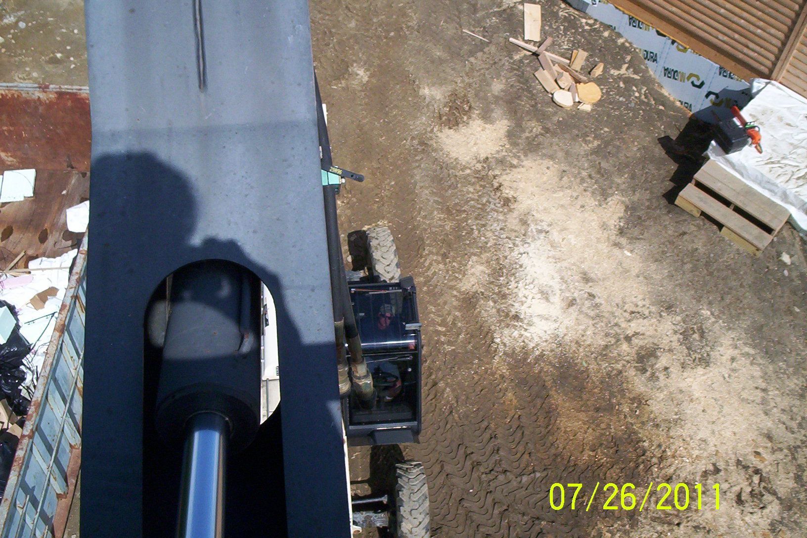 Overhead view of a blue vehicle beside a dirt lot with a person near stacked blocks on the right