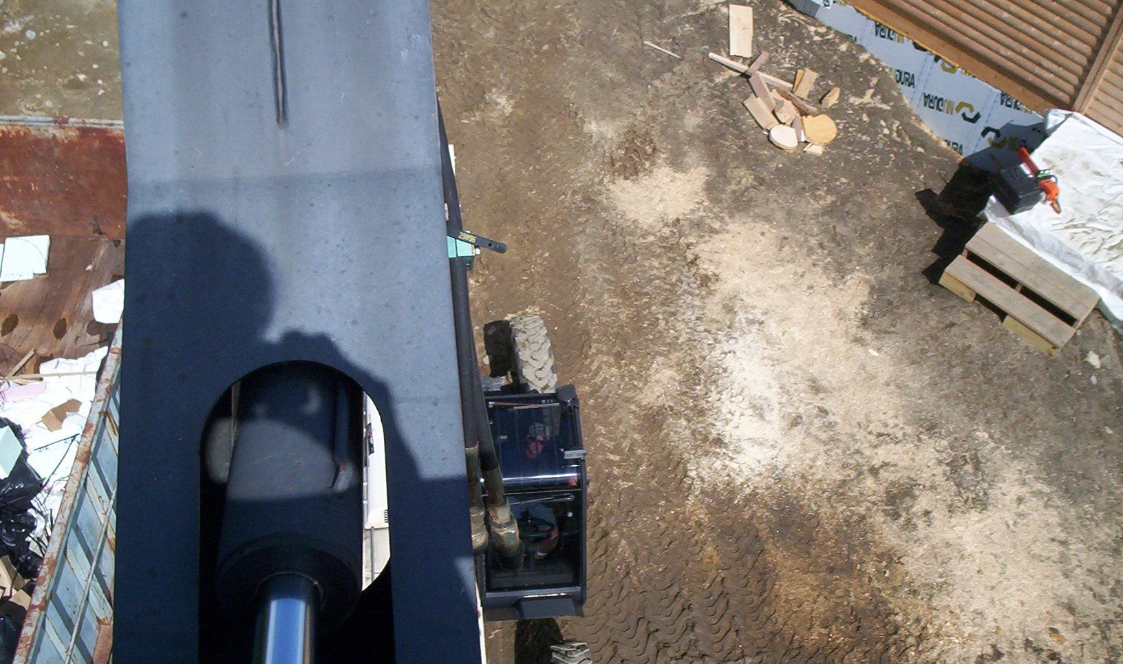 Aerial view of a rooftop and dirt yard, with a person near concrete blocks on the right.