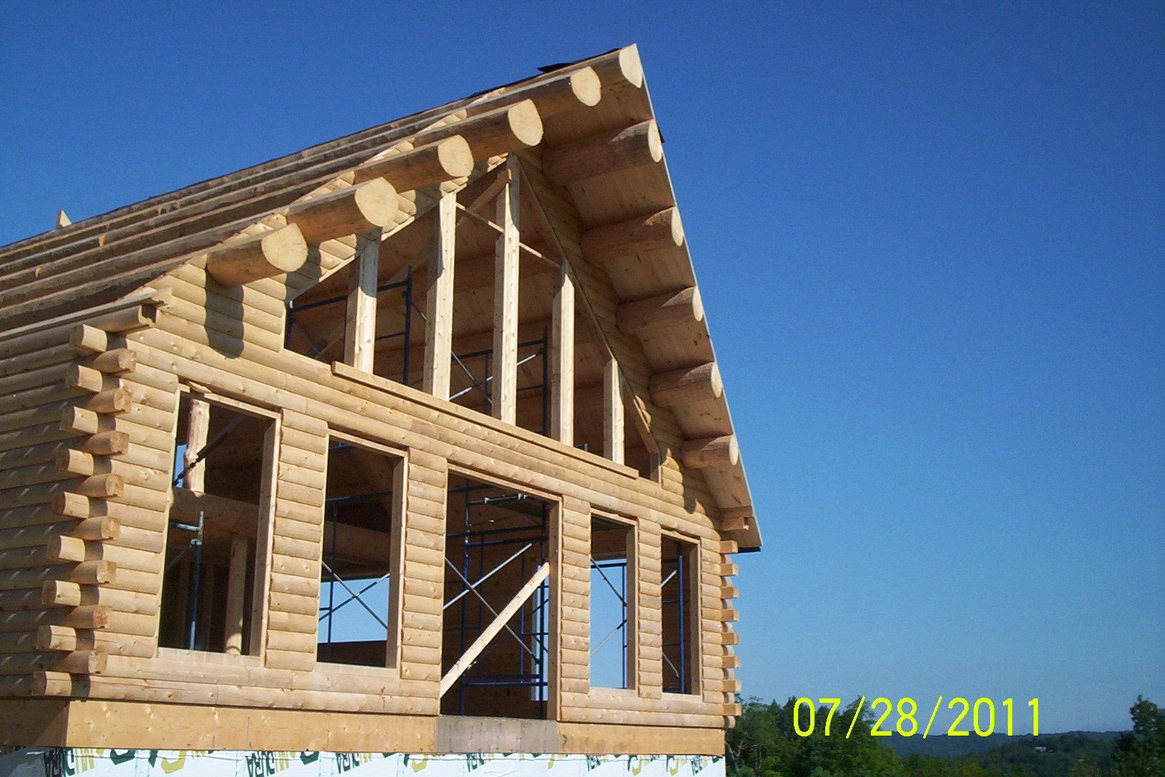 Partially built log house with exposed framing and blue sky behind it
