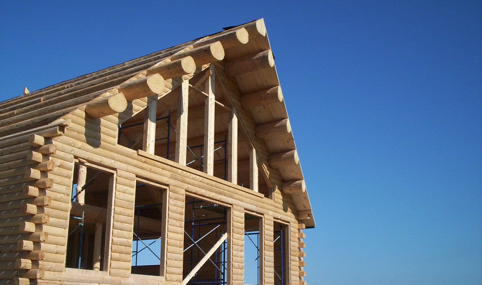 Partially built wooden house frame against a clear blue sky