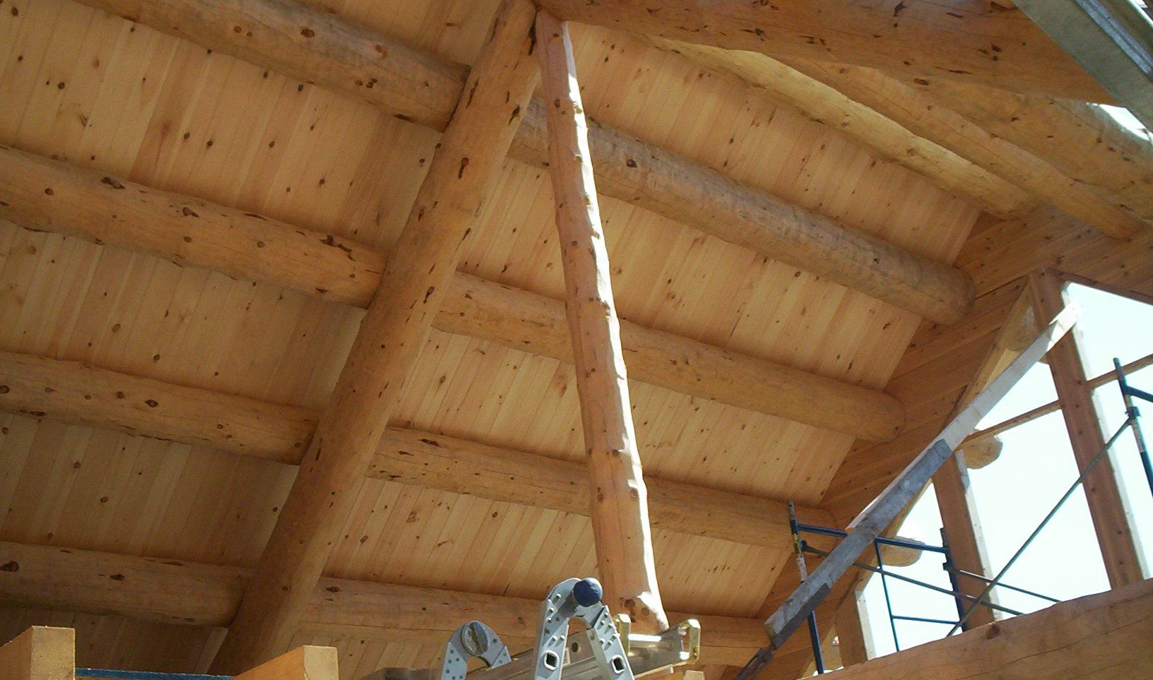 Wooden vaulted ceiling with exposed beams, a hanging light fixture, and a ladder at the right side.