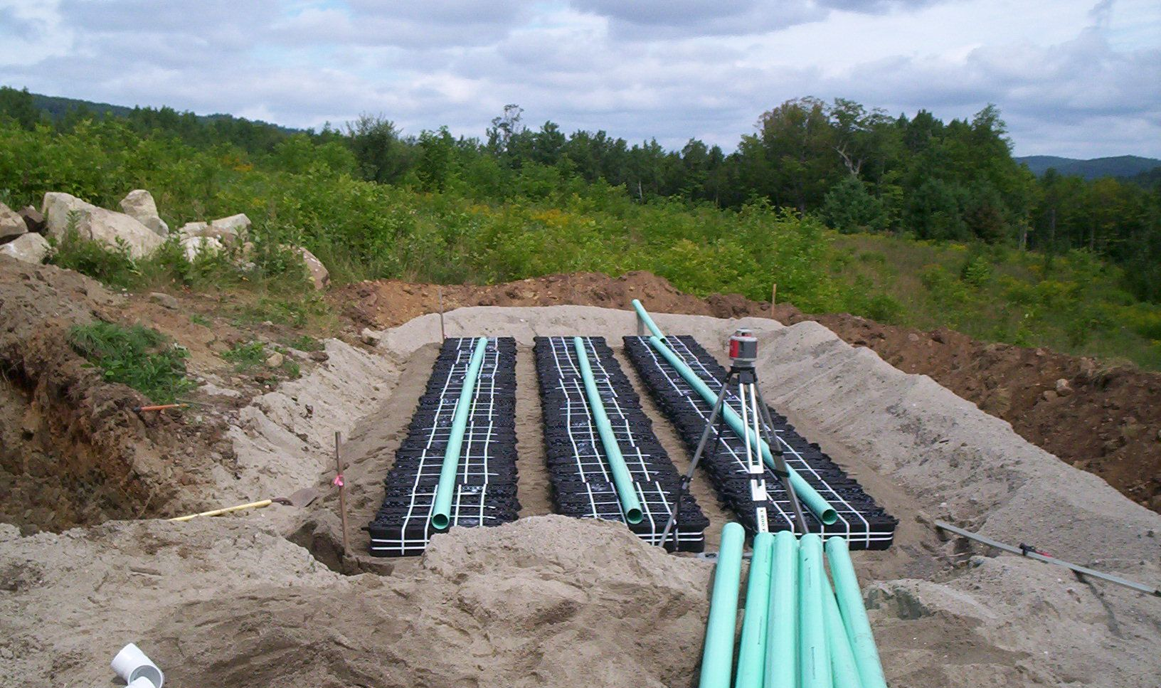 Trenches with black pipes and blue conduits laid in sand at a construction site