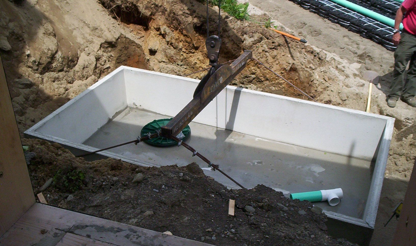 Worker installing white fiberglass tank in a muddy excavation site