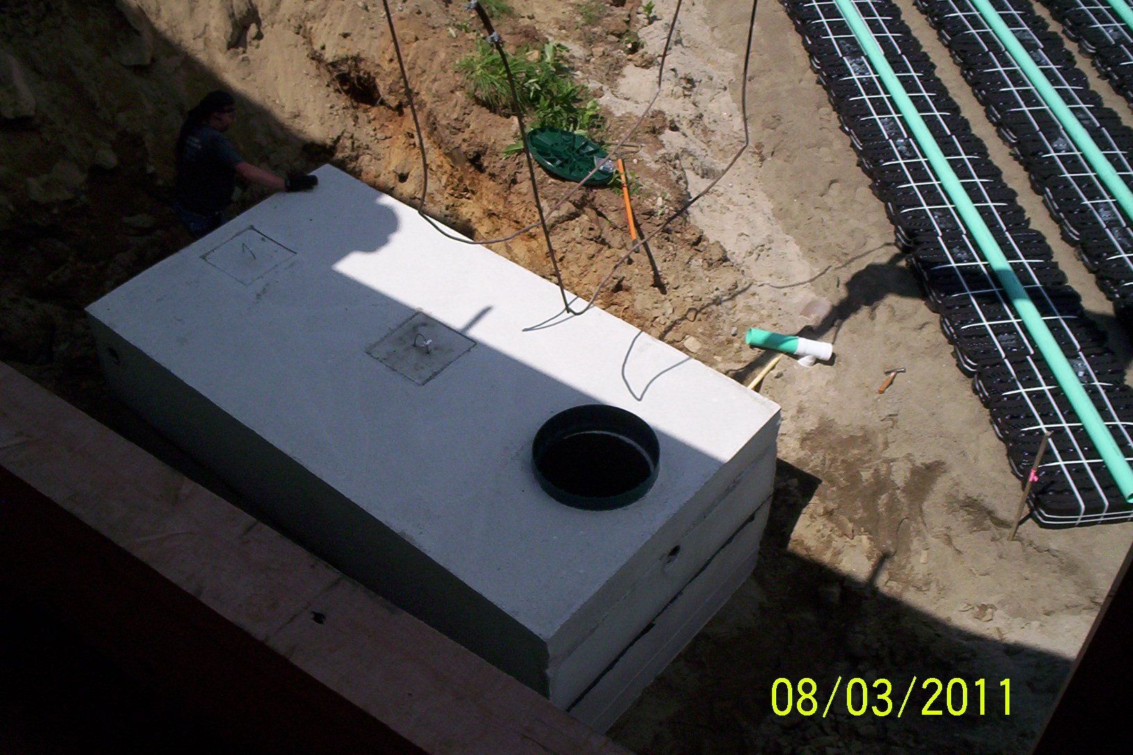 Concrete utility box beside roadwork trench with black cables and a date stamp.