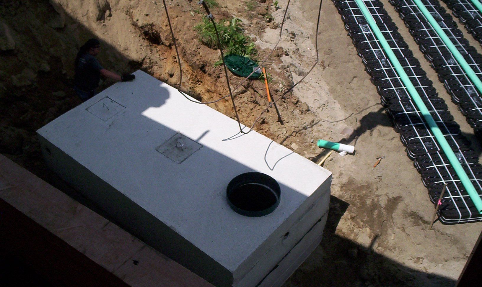 Gray utility box in a dirt trench beside black cables and pipes at a construction site