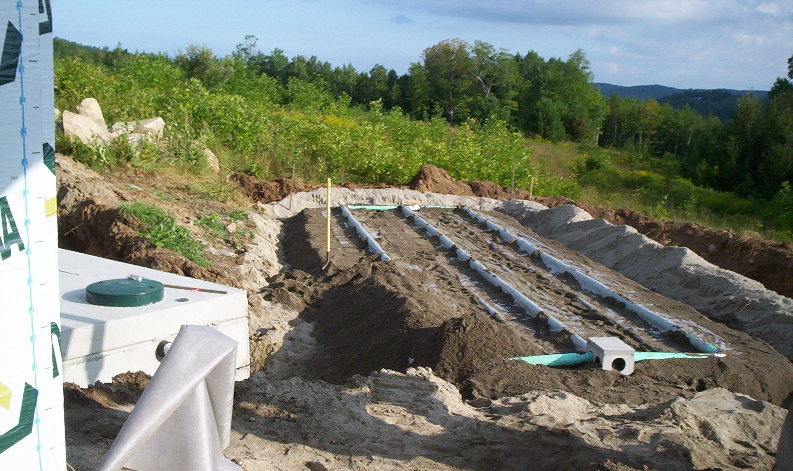 Outdoor construction site with trenches, pipes, and gravel beside a white building under a clear sky