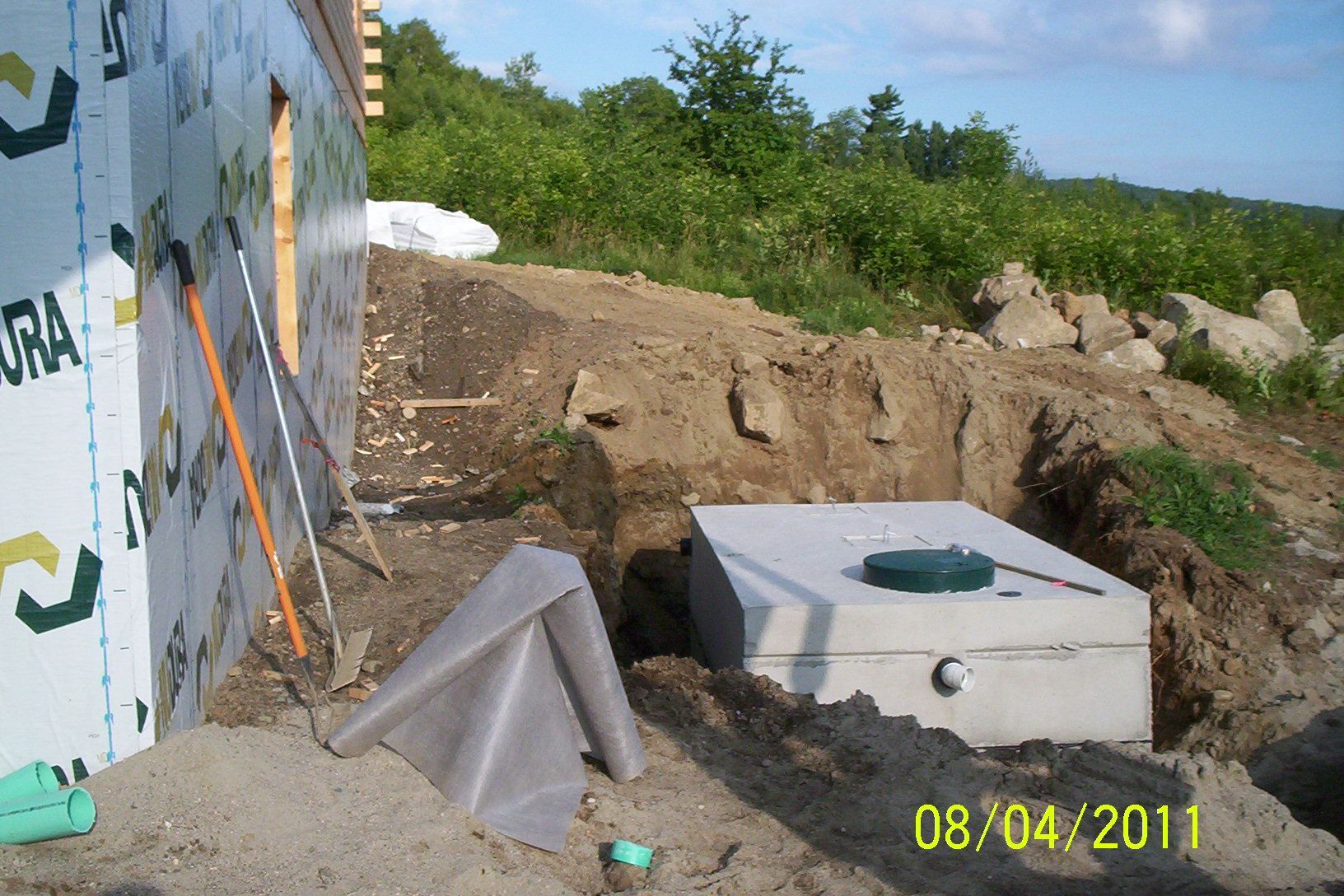 Outdoor construction site with concrete foundation, dirt mound, and a partially built wall under a blue sky