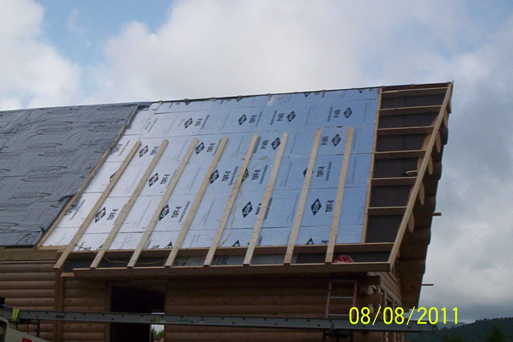 Roof under construction with blue insulation panels and wooden framing under a cloudy sky