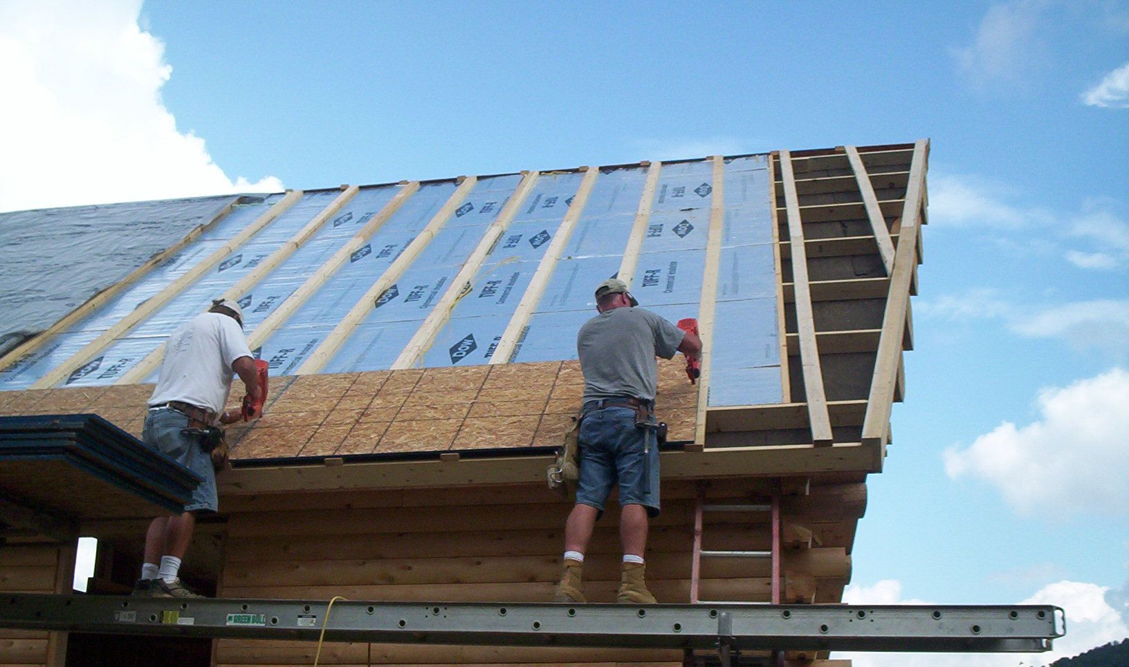 Two workers installing wooden roof sheathing on a house under construction