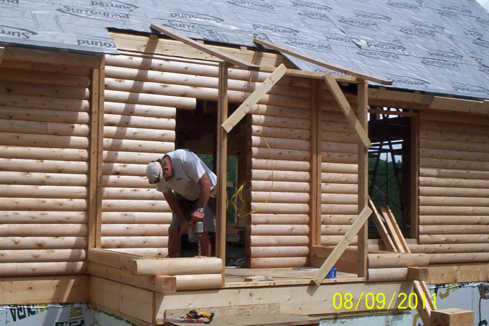 Worker framing a log cabin wall at a construction site