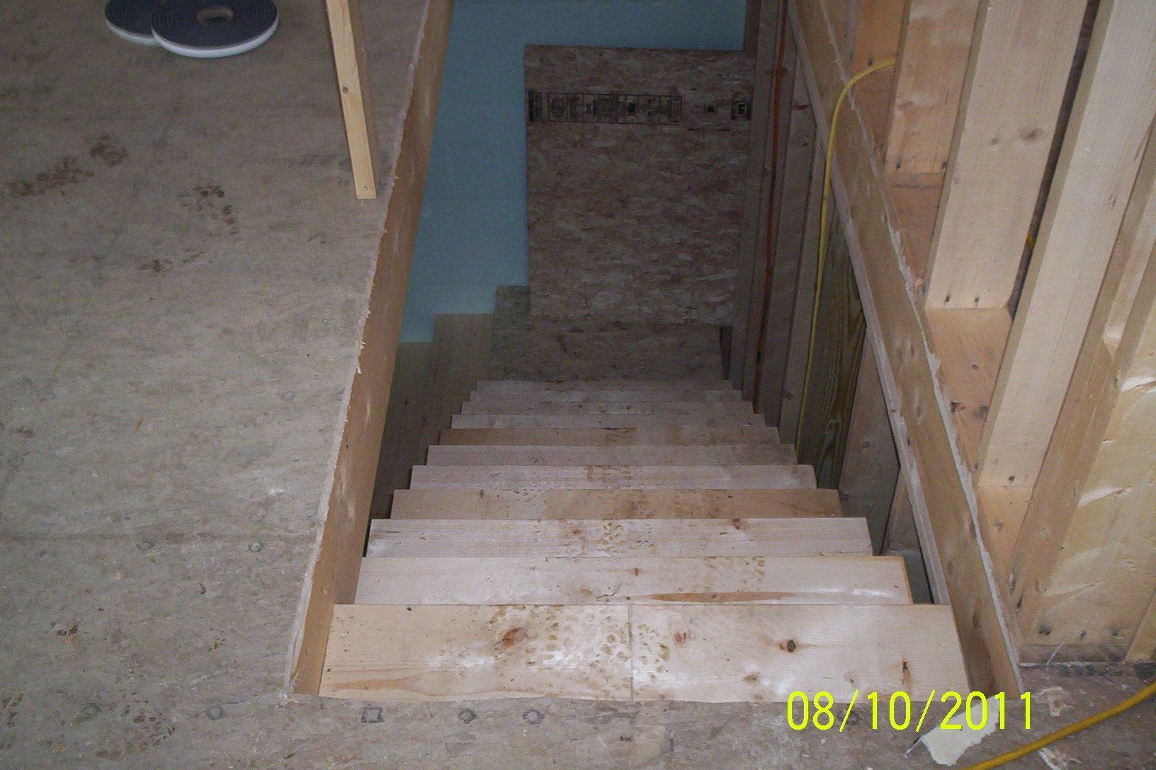 Unfinished basement stairwell with wooden steps and exposed framing leading downward