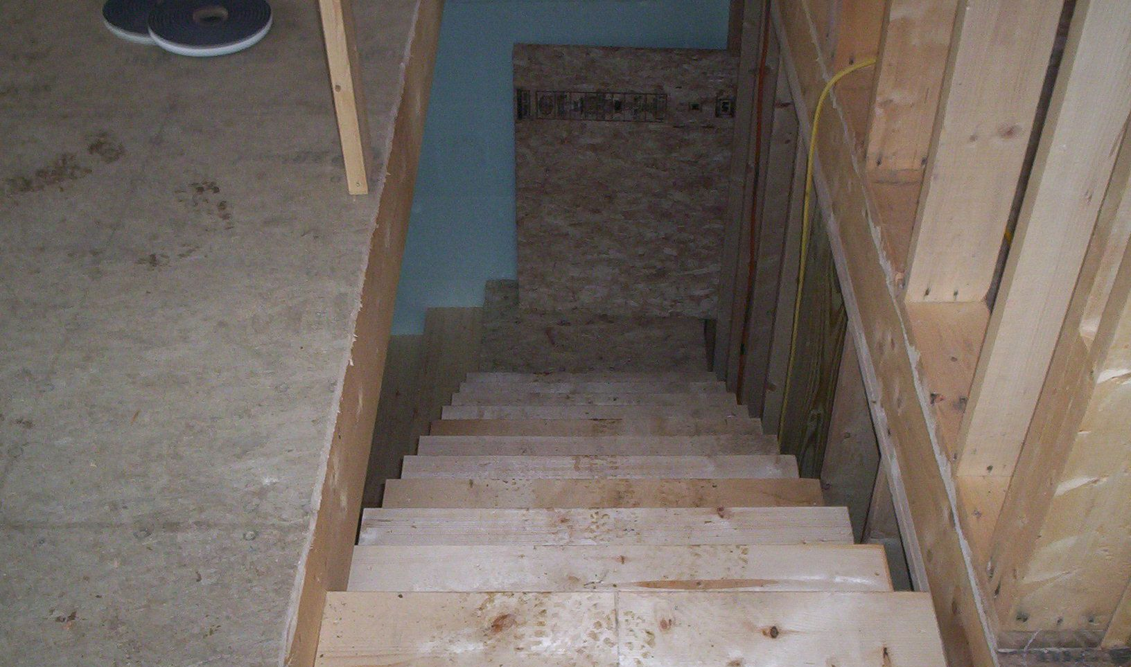 Narrow unfinished basement stairs with wooden steps leading down to a concrete floor