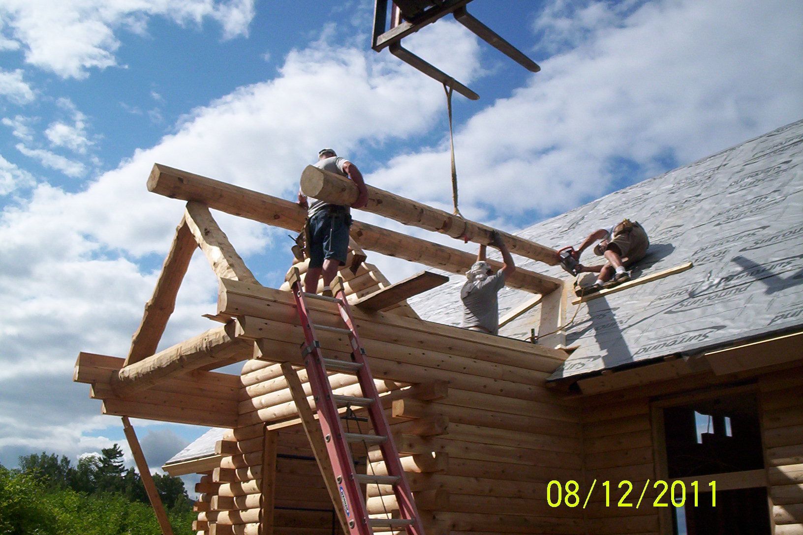 Two workers building a wooden roof frame on a house under a blue sky