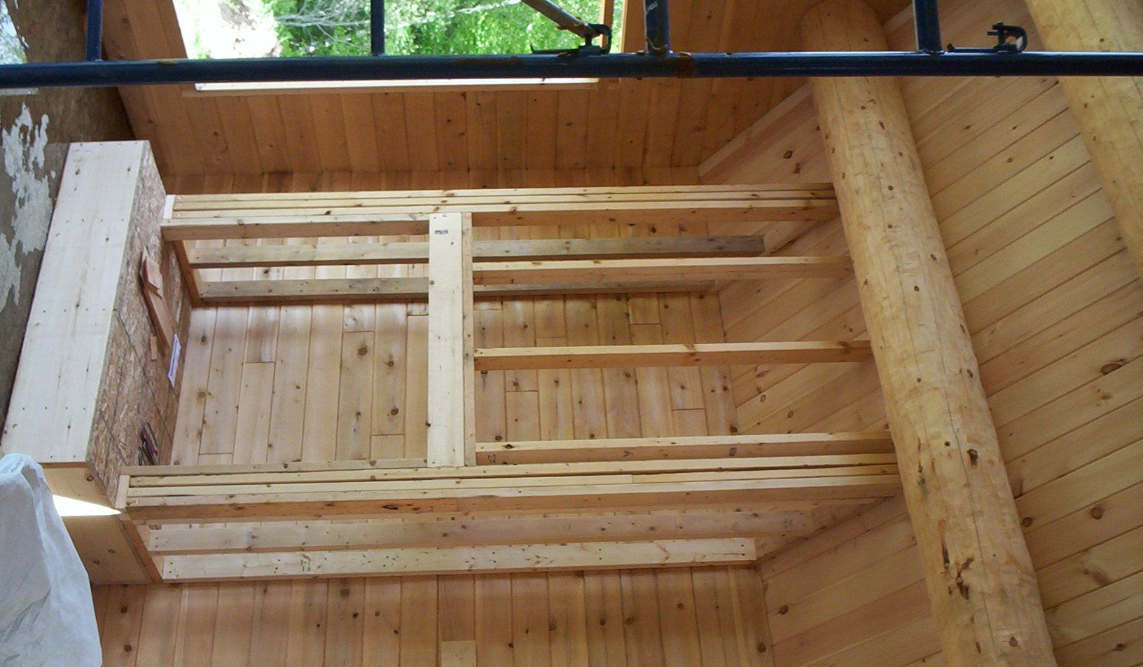 Wooden cabin interior with unfinished log walls, ceiling beams, and a small window near the top