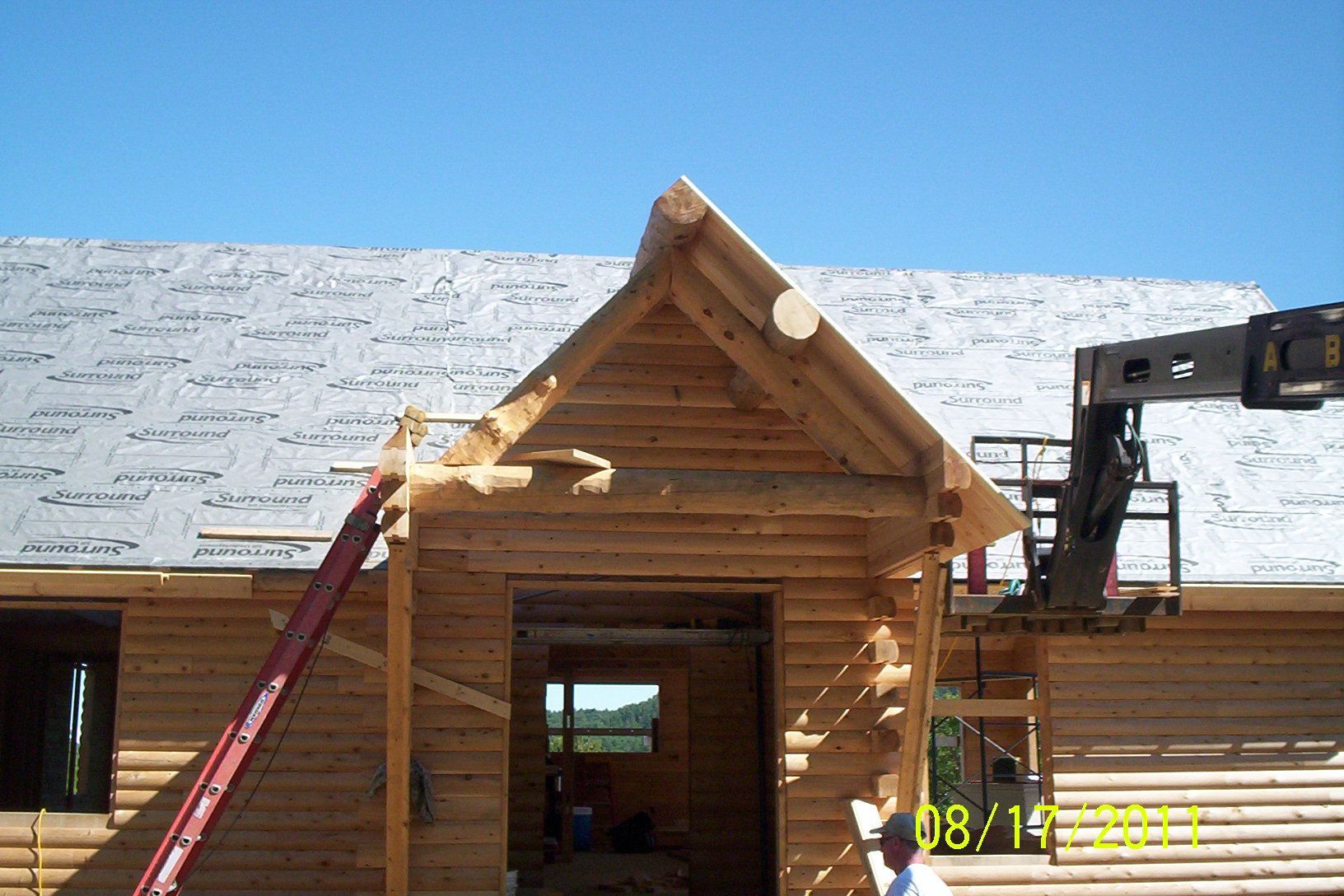 Workers installing roof trusses on a wooden building under construction, with a crane on the right.