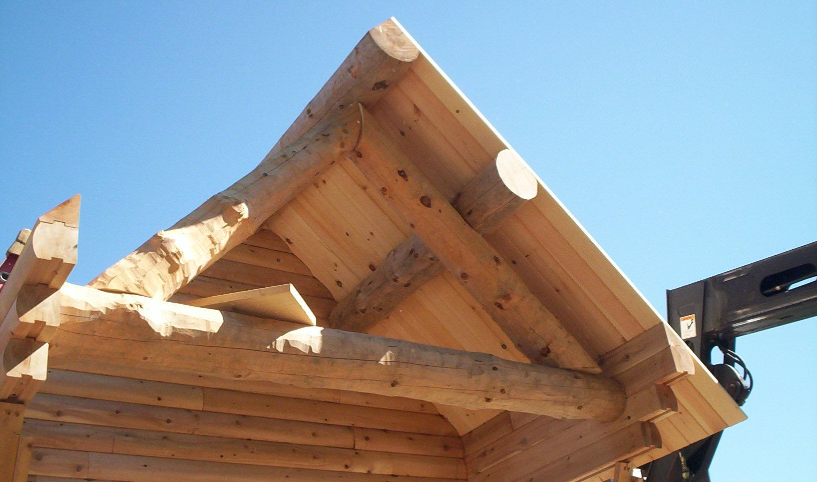 Wooden log cabin roof frame under construction against a clear blue sky