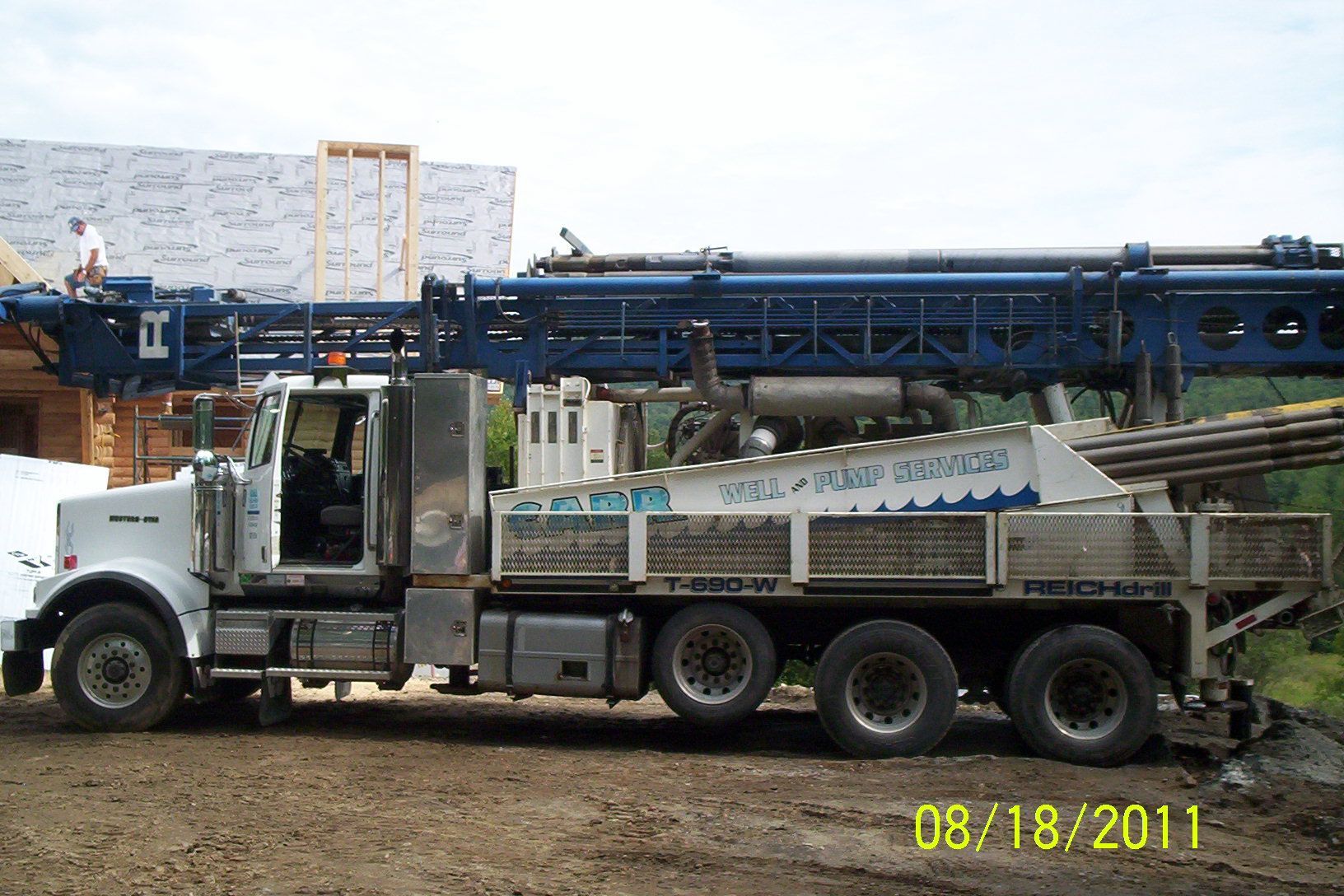 White dump truck loaded with gravel in an industrial yard, with a blue conveyor structure behind it.