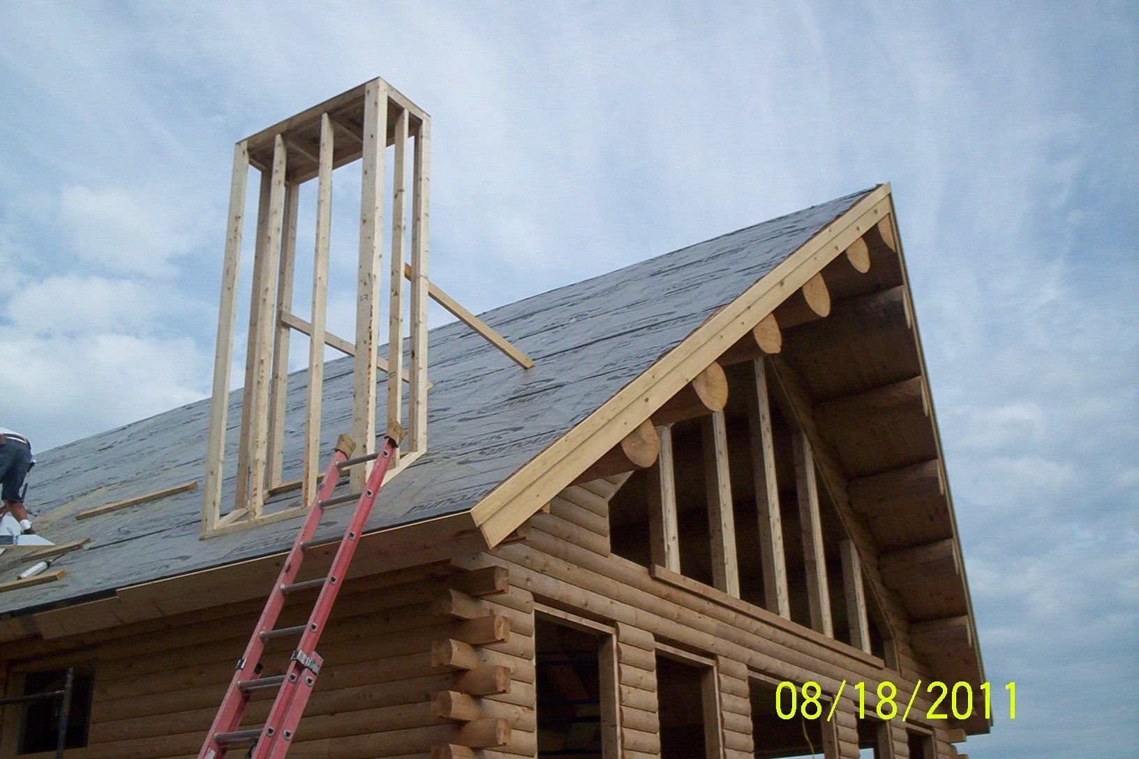 Roof under construction with red ladder and unfinished dormer framing against a cloudy sky