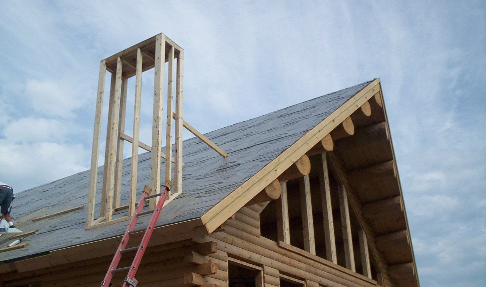 Roof under construction with a wooden dormer frame and red ladders on a log cabin roof