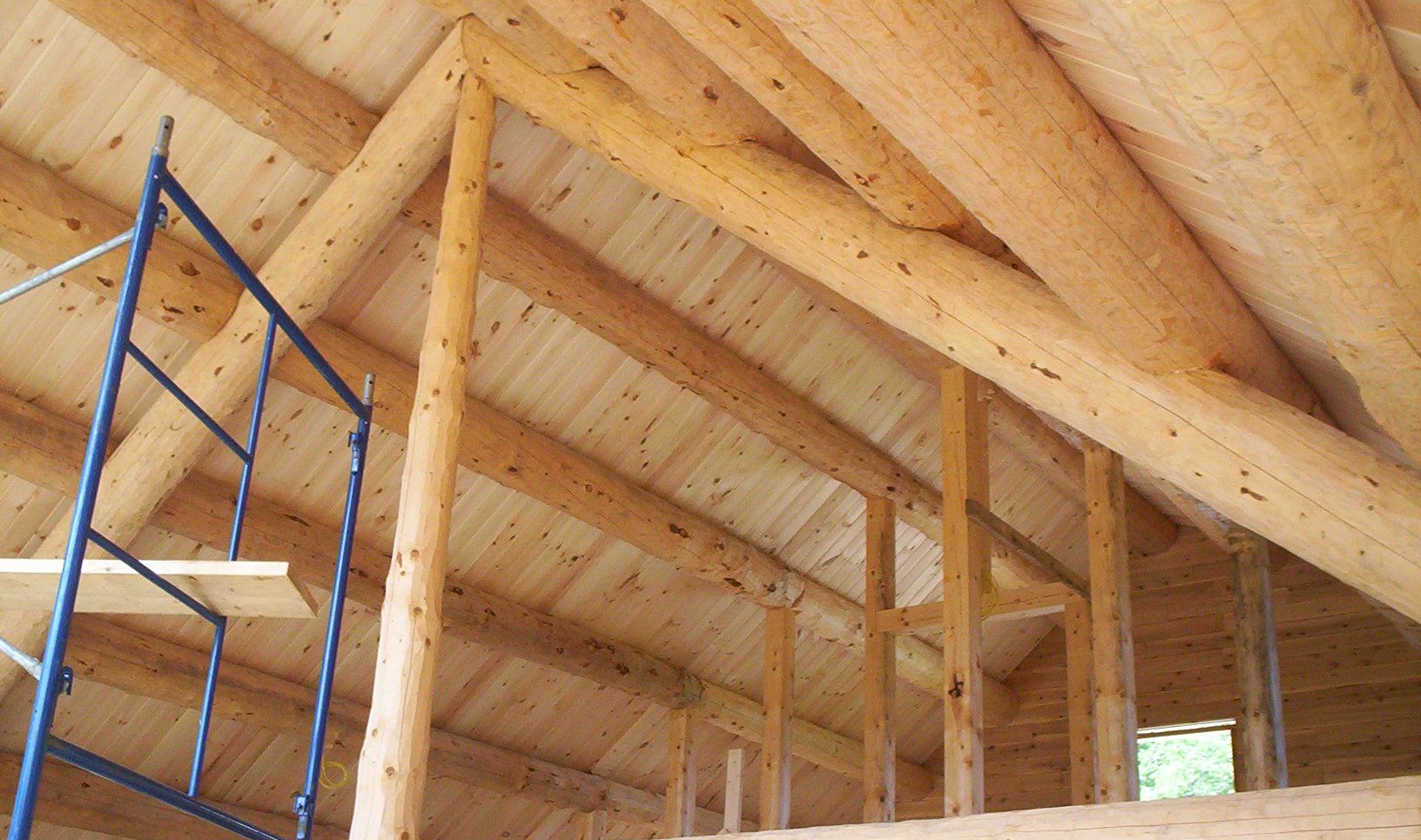 Wooden attic interior with exposed rafters and blue scaffolding on the left side.