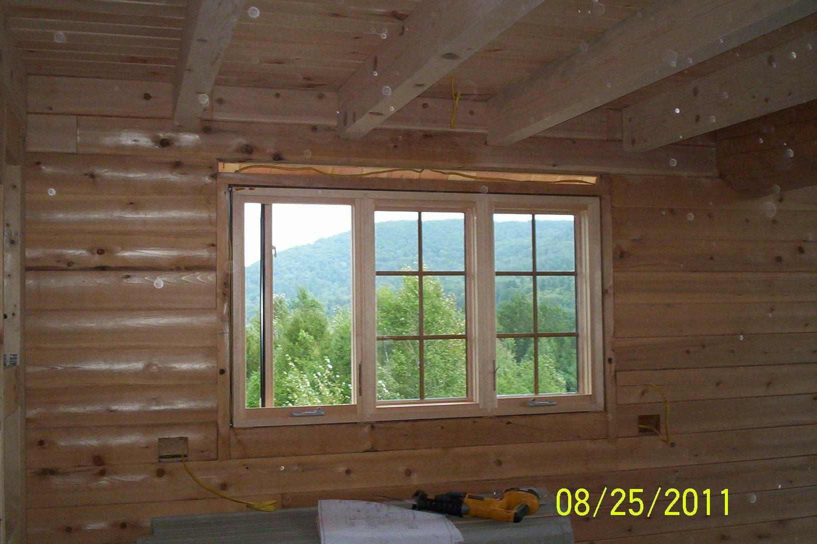 Wood-paneled cabin interior with a window overlooking green hills and trees