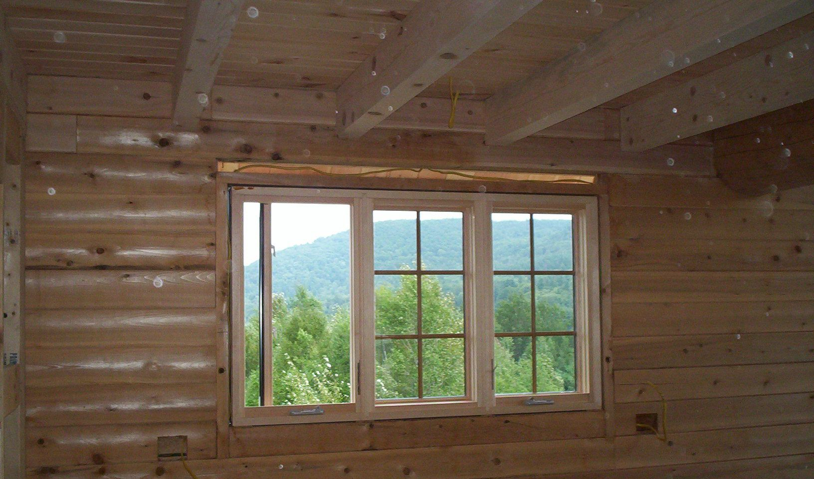 Wooden cabin interior with a large window overlooking green mountains and trees