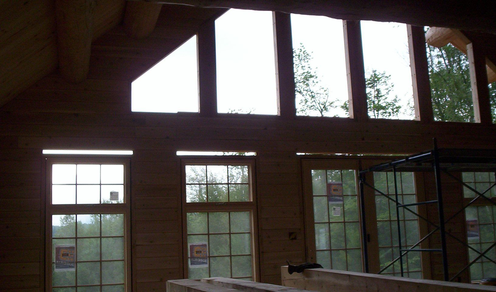 Sunlit wooden room with large windows and exposed beams, looking out to trees
