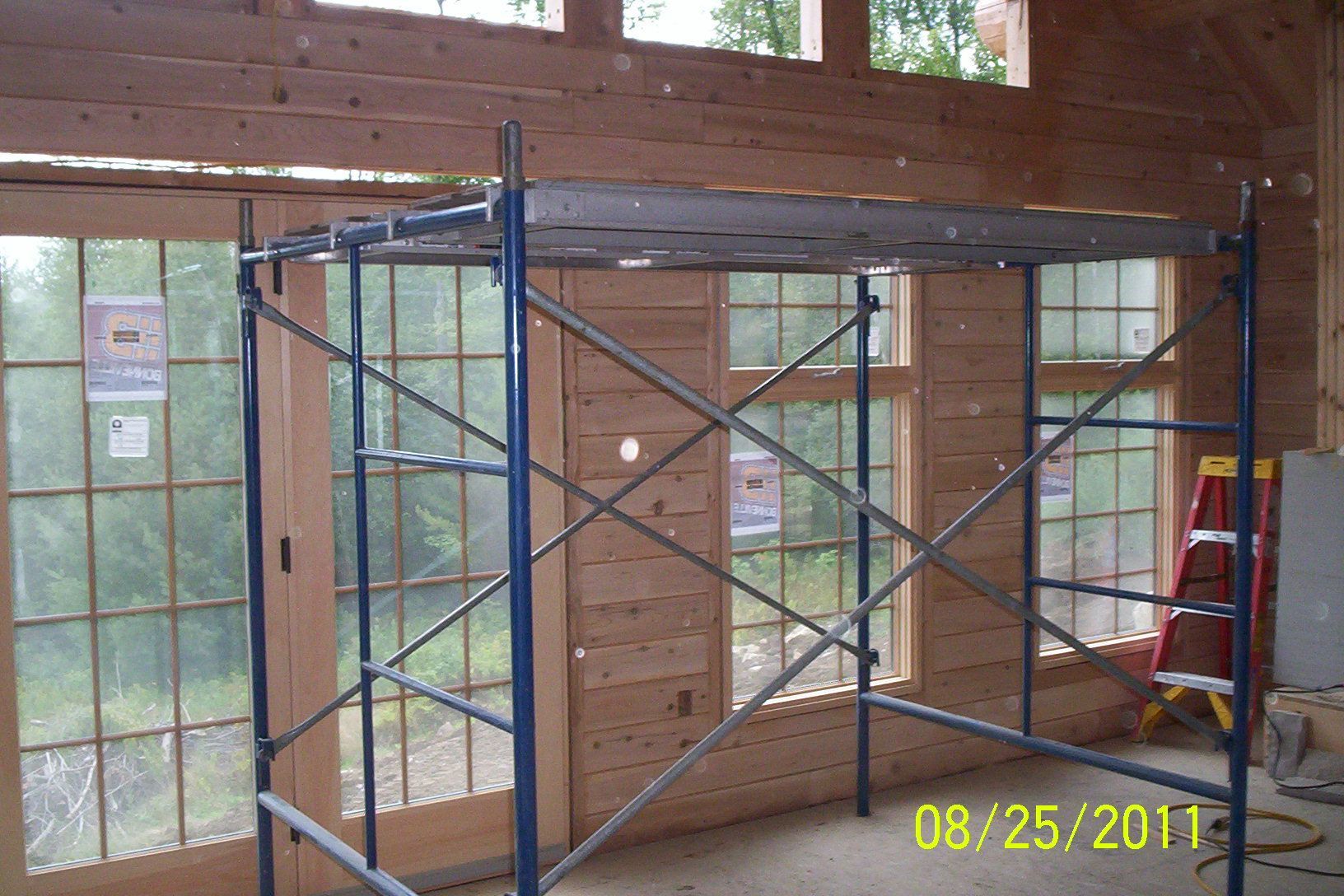 Scaffolding inside an unfinished room with wooden beams, large windows, and a red ladder.