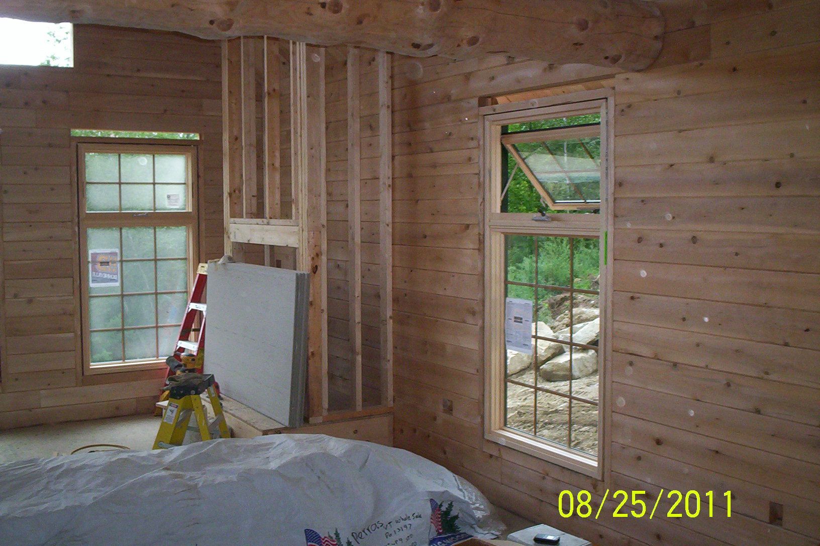 Unfinished room with exposed studs, windows, a ladder, and covered furniture; dated 08/25/2011.