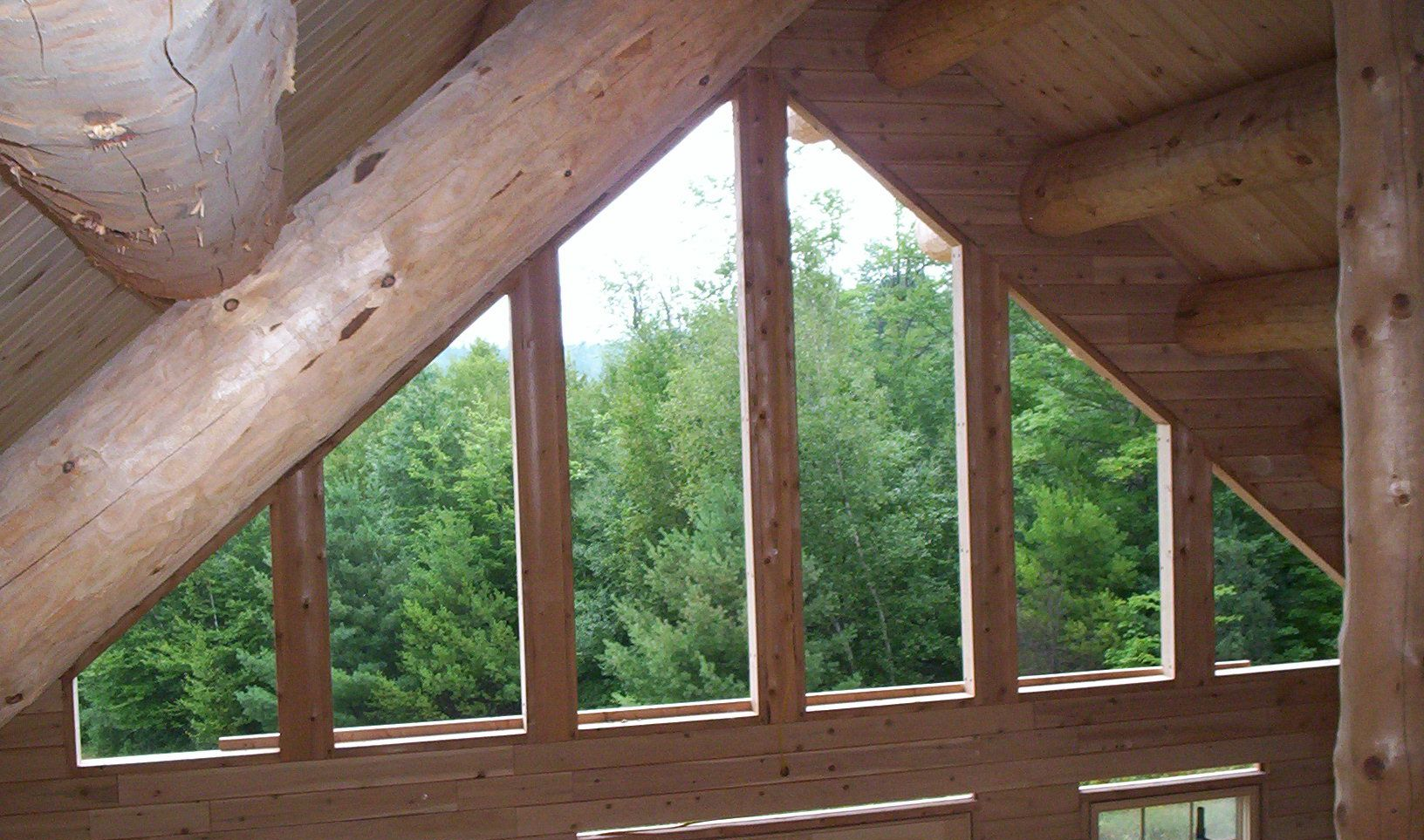 Wooden log cabin window framing a view of green trees outside