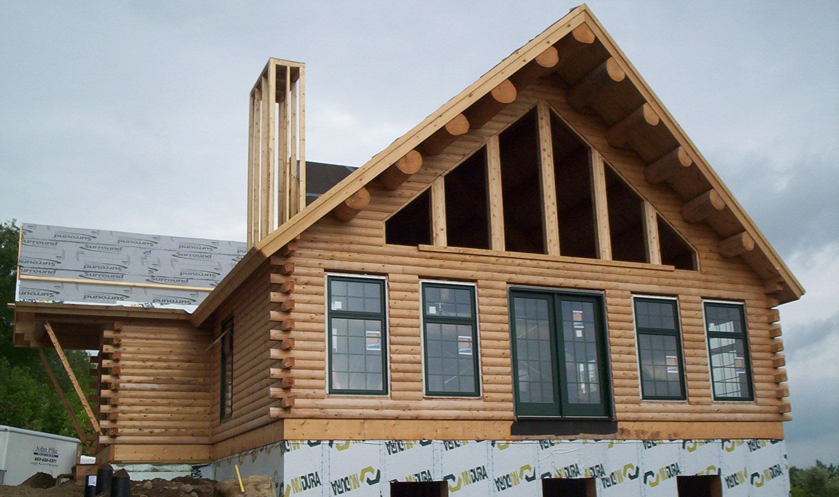 Wood-sided cabin with unfinished roof and chimney under construction beside a snowy mountain